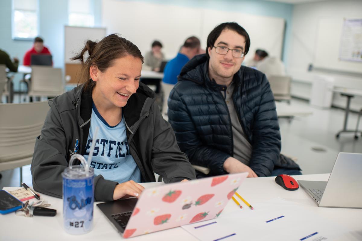 Two Economics majors looking at a laptop smiling one wearing WSU shirt and the other a black coat.