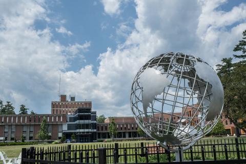 Globe on the campus green in the blue skies and white clouds with the Campus Center in the background