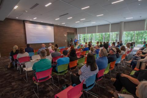 Multi-colored chairs hold new students and their Champions while presentations about new student orientation are given via a projector.