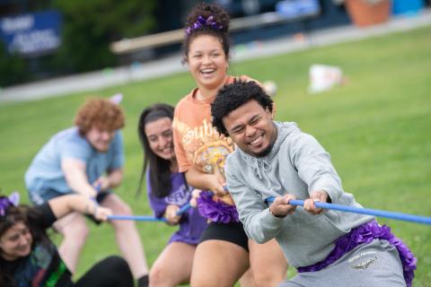 Five students play tug of war with a blue rope