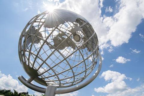 A stock photo of the campus globe. The sun shines above and there are clouds in the sky.