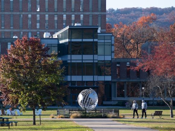 A campus stock photo of the globe and Ely in mid-fall. Red and green trees are on either side of the globe, and two figures are walking in the distance.