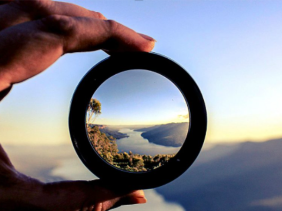 a left hand holding a lens over a view of a river in a valley