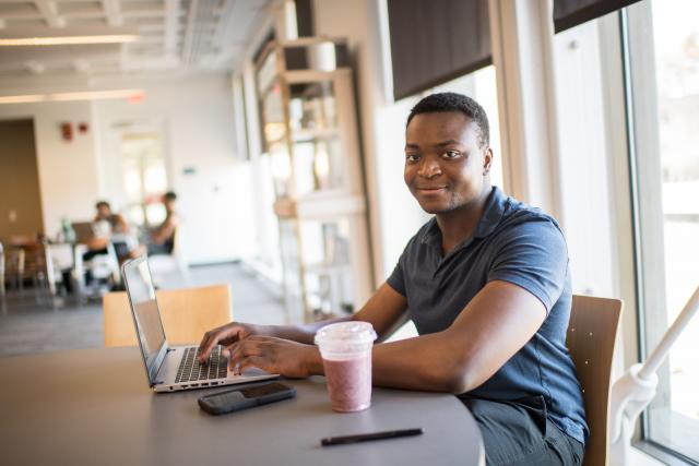 Smiling student looking at camera while working on laptop in the campus center