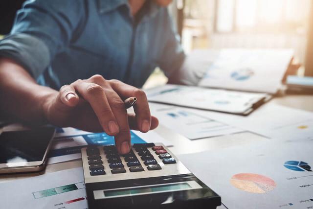 A person analyzing financial documents and using a calculator.