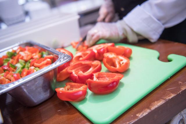 Red and green peppers being chopped up on green cutting board.