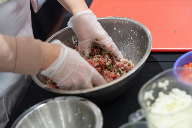 Cooking with Maria Class featuring Maria making Greek meatballs. Photo shows the meat and spices in a mixing bowl.