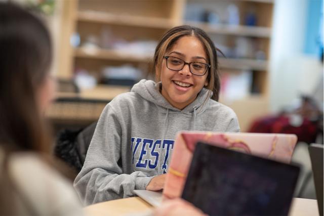 Two education majors at Westfield State University smile while working on their laptops in a study area.