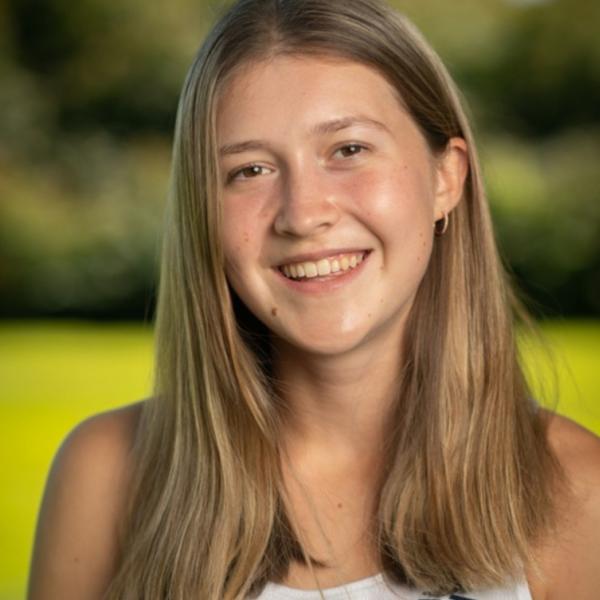 Student tour guide Shea Hamel. She is smiling and standing in an open field, with the background blurred behind her. 