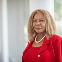 Dr. Linda Thompson in a red suit and standing in front of an open and bright mirror.