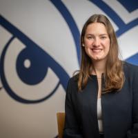 Elin-Maree Krupa, an international transfer student from Germany. She poses in front of a blue and white Owl mural and wears a dark blue coat jacket.